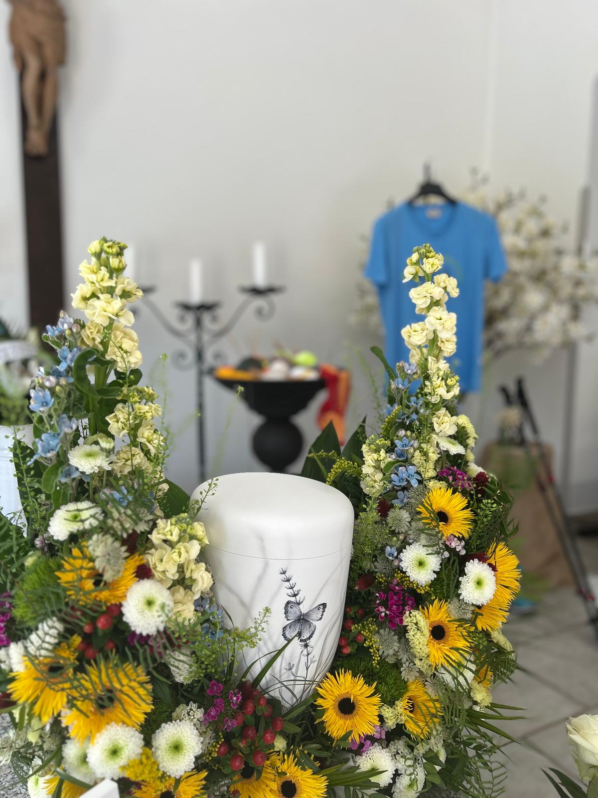 Urne mit Schmetterlingsmotiv in einem Gesteck aus Sonnenblumen und Sommerblumen