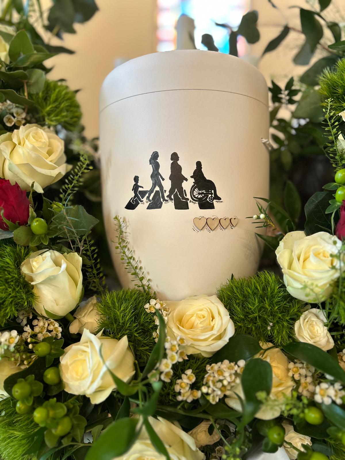 Weiße Urne mit gemalter Familien-Silhouette in einem Kranz aus weißen Rosen